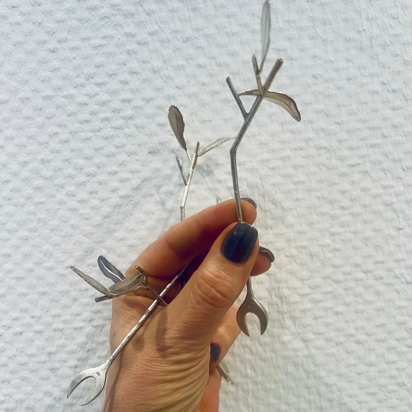 Hand hält handgeschmiedeten Oliven-Pikser aus 925 Silber mit Olivenblatt-Design vor hellem Hintergrund