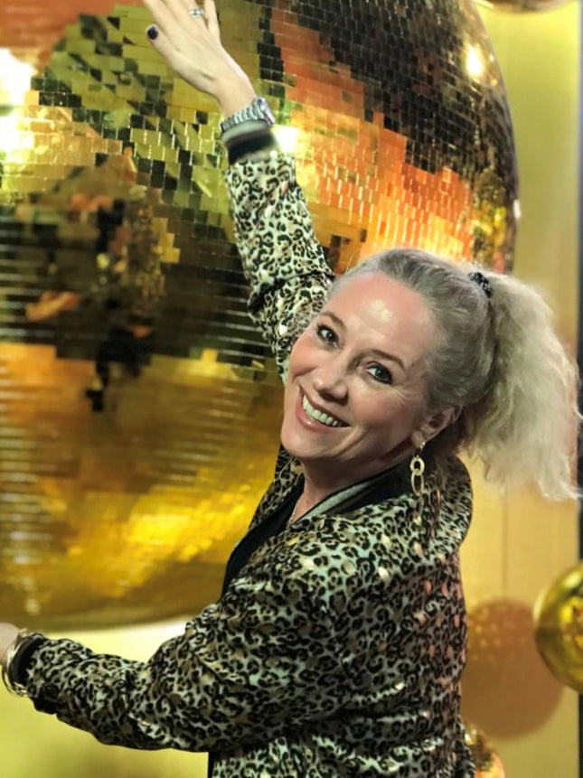 Andrea Quast vor einer goldenen Discokugel bei einer Atelier Q Veranstaltung – mit Leopardenjacke und Armreif