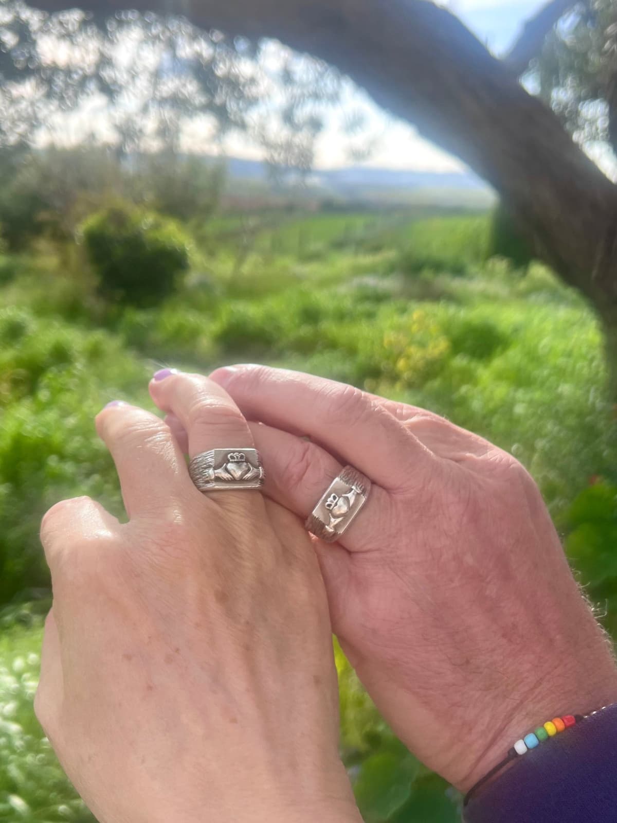 Zwei handgeschmiedete Claddagh Ringe aus 925er Silber – getragen an den Händen, Symbol für Liebe, Treue und Freundschaft, fotografiert in der Natur von Irland.