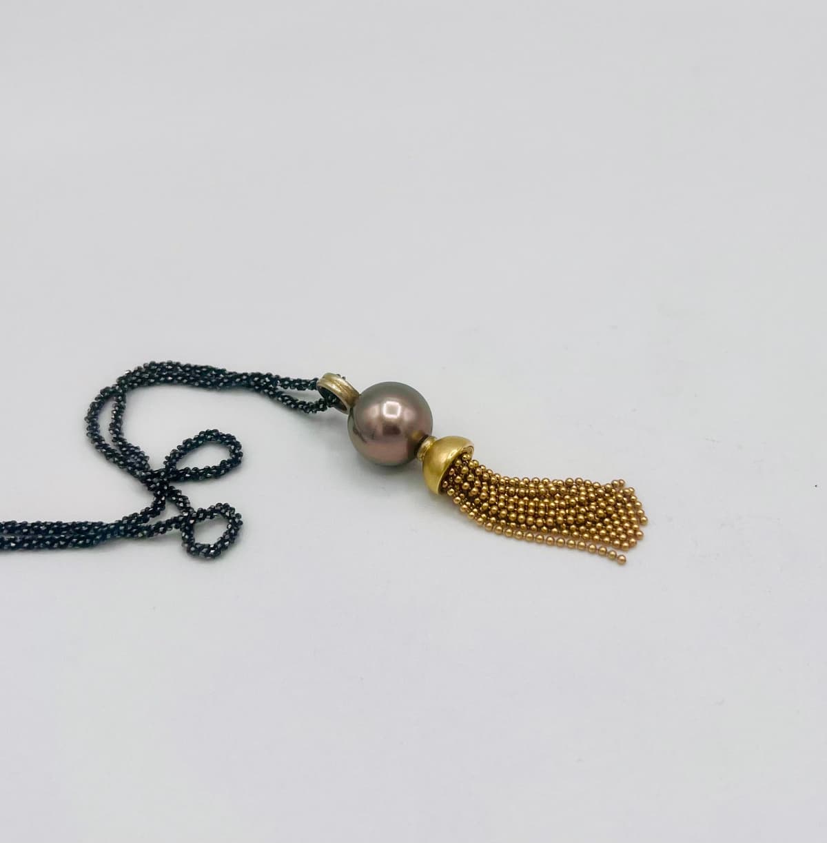 „Anhänger ‚Star of the Sea‘ mit Tahitiperle und 750er Gelbgold, veredelt mit frei beweglichen, zarten Kugelketten unter der Perle – an geschwärzter Silberkette.“