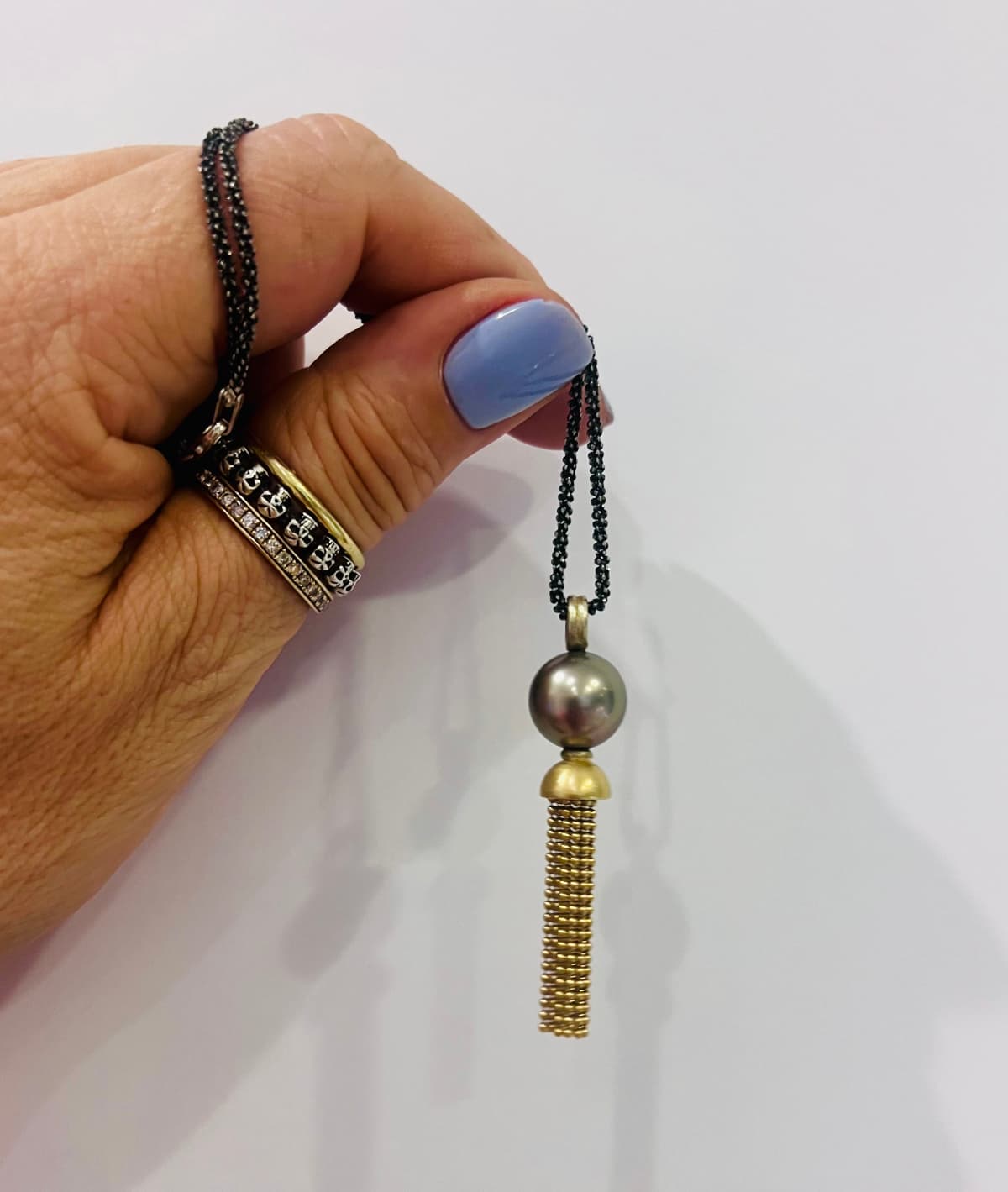 „Handaufnahme des Anhängers ‚Star of the Sea‘ mit Tahitiperle, 750er Gelbgold und frei beweglichen Goldkugelketten – gezeigt an geschwärzter Silberkette.“