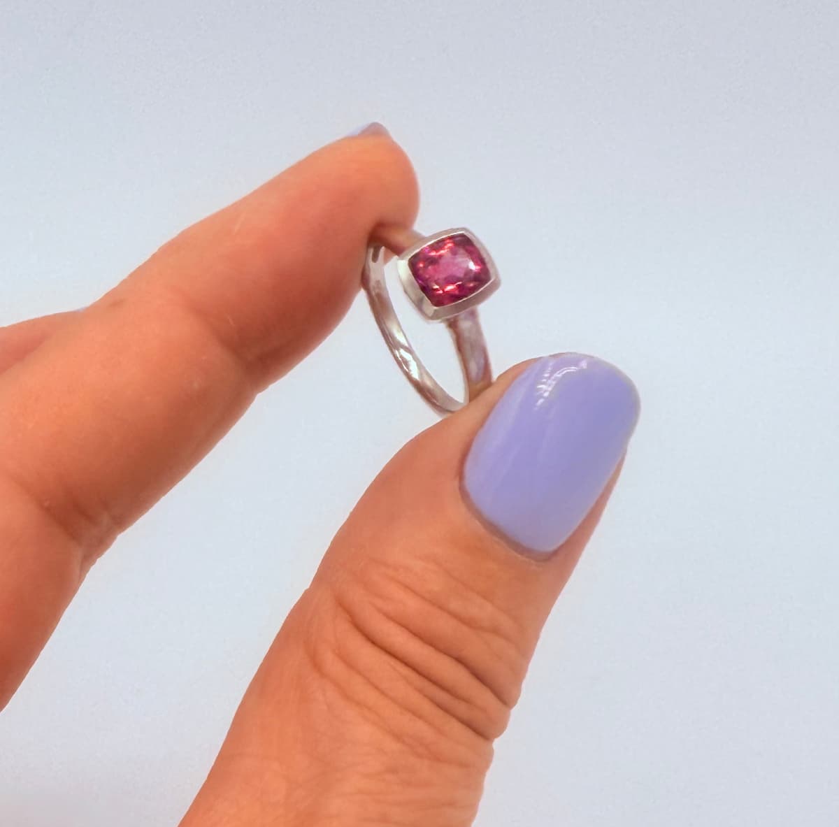 Solitärring aus Platin mit Rhodolit – handgeschmiedet im Atelier Q. Moderner Ring mit leuchtend pinken Edelstein, zwischen 2 Fingern gehalten.