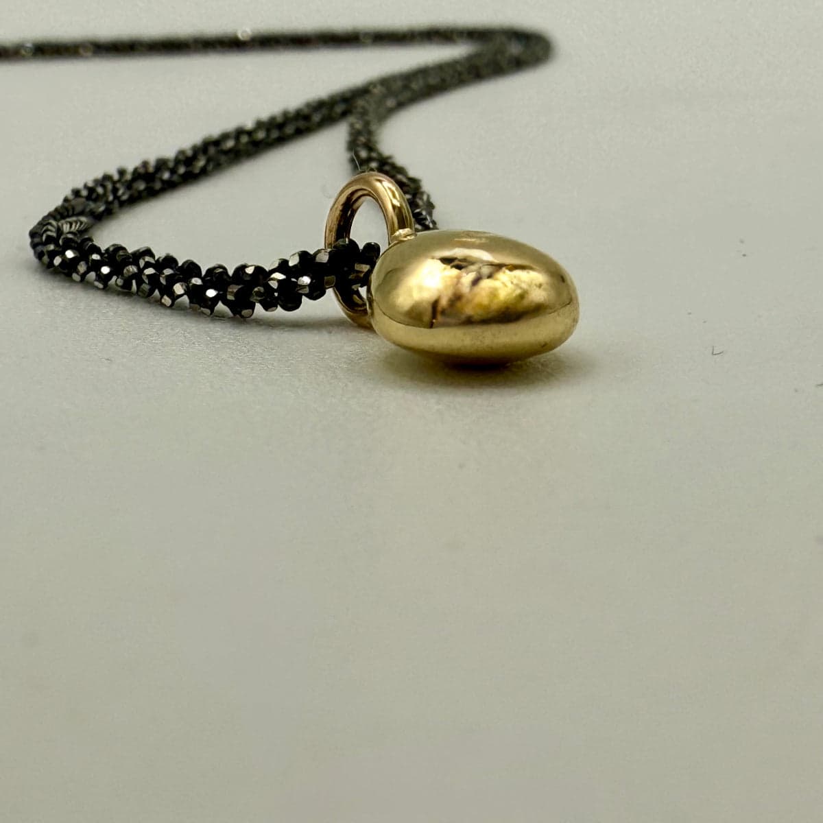 Nahaufnahme von einem Gold Nugget, liegend,mit geschwärzter Silberkette. Unikatschmuck aus Köln. Atelier Q