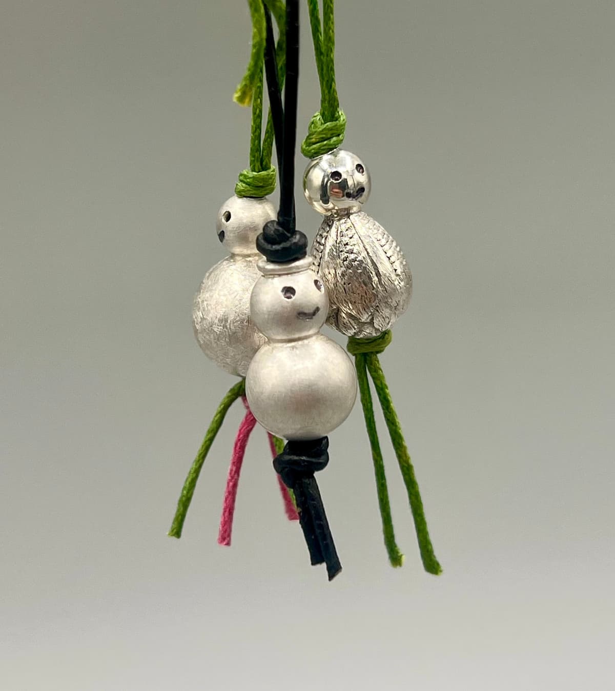 Handgefertigte Lucky Charms aus Silber – kleine Anhänger aus Kugeln im Stil früher Holz-Glücksmännchen, an bunten Bändern präsentiert.